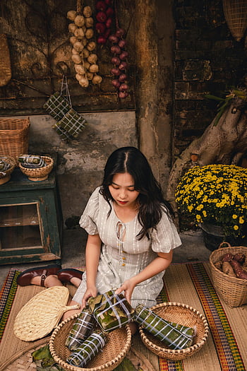 woman, woven carpet, Banh Tet, Banh Chung, vegetables, rustic setting, baskets, traditional food, Vietnamese cuisine, cultural scene, indoor setting