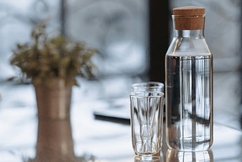 clear glass bottle, water bottle, drinking glasses, carafe, cork lid, reflective surface, still life, elegant glassware, reflective table, indoor decor, simple setup