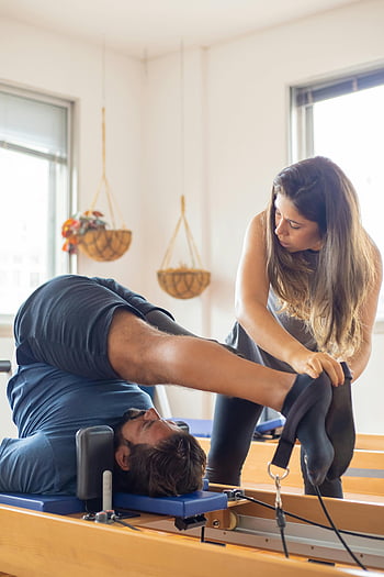 Esercizio di Pilates, uomo che fa pilates, istruttore che assiste, allenamento in palestra, allenamento per la flessibilità, esercizio di riabilitazione, Pilates Reformer, allenamento fisico, allenatore personale, attrezzature per l'esercizio, allenamento indoor