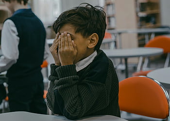 boy covering face, child hands covering face, bullying in school, school setting, emotional distress, sad child, classroom environment, young student, school bullying, emotional pain, school child