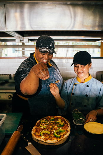 Příprava pizzy, Kuchaři připravují pizzu, restaurace kuchyně, Muž a žena vaření, pizza zálivky, Radostí kuchaři, Rušná kuchyně, výroba pizzy, Spolupráce šéfkuchaře, Pizza v kuchyni, Kuchaři pizzy