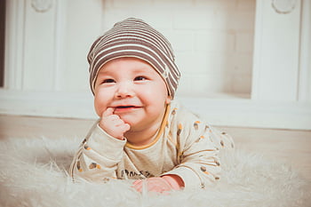 usmívající se dítě, kousavý prst, pruhovaná beanie, Útulné oblečení, měkký koberec, uvnitř, dětské fotografie, šťastné dítě, baby móda, Dětské doplňky, dětský životní styl