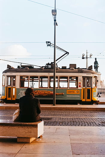 vintage tram, Lisbon street, person sitting, bench, foreground, tram passing, vintage transportation, urban scene, cityscape, historical tram, Lisbon Portugal