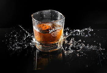 Jack Daniel-printed glass, whiskey, ice, splash, dynamic shot, Jack Daniel's brand, drinking glass, black background, high contrast, liquid motion, reflections