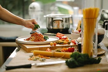 cozy kitchen, homemade spaghetti, garnished parsley, adding greens, pasta dish, cooking process, fresh ingredients, kitchen setting, food preparation, healthy meal, culinary scene