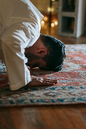 man praying, white thobe, red and blue rug, traditional attire, indoor prayer, faith and devotion, religious practice, cultural tradition, spiritual devotion, prayer rug, man bowing