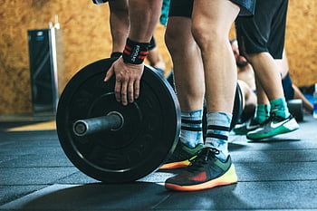 person holding black weight plates, close-up workout, gym exercise, barbell lifting, fitness training, weightlifting, gym workout, athletic shoes, gym floor, weight plates, gym equipment