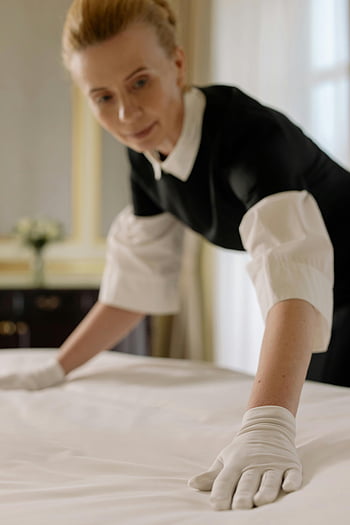 hotel housekeeper, bedmaking, luxury hotel room, hospitality expertise, elegant arrangement, professional service, clean bed sheets, indoor hospitality, hotel staff, tidy room, comfortable lodging