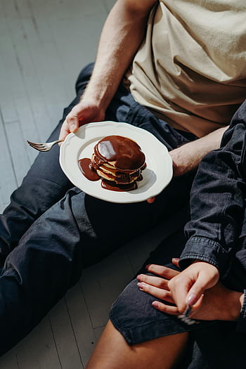chocolate pancakes, morning indulgence, high-angle view, drizzled chocolate syrup, person holding plate, breakfast treat, sweet breakfast, chocolate drizzle, pancake stack, indulgent breakfast, chocolate topping