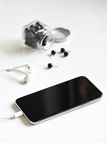 Black iPhone 7, minimalist arrangement, smartphone, earbuds, jar, pushpins, white background, tech accessories, modern gadgets, clean design, product photography