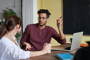 man holding pen, collaborative discussion, team meeting, office setting, colleagues, laptop, coffee cup, professional environment, workplace interaction, business meeting, office discussion