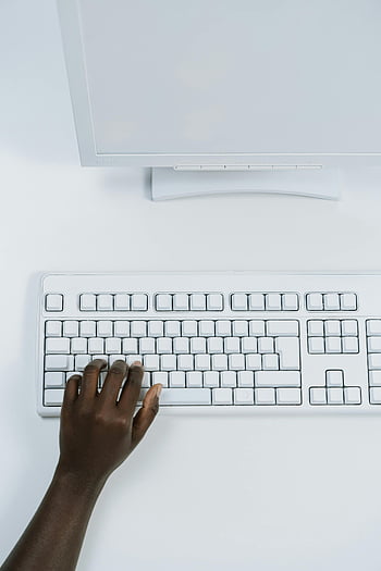 white computer keyboard, hand typing, close-up, white surface, computer monitor, ergonomic keyboard, workspace, minimalist setup, office equipment, technology, productivity