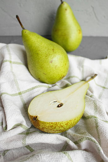 green pears, striped cloth, ripe fruit, juicy fruit, high-angle view, fresh pears, table setting, sliced pear, whole pears, cloth texture, fruit photography