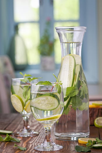 clear glass bottle, lemon cucumber lemonade, refreshing detox drink, cucumber lemon mint, glass pitcher, glasses, mint leaves, lemon slices, cucumber slices, wooden table, natural light