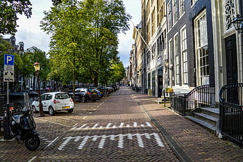 Amsterdam, centrul istoric, strada pavata, arhitectură istorică, mașini parcate, zi insorita, strada liniștită, oraș îmbătrânit, canal, copaci, felinar