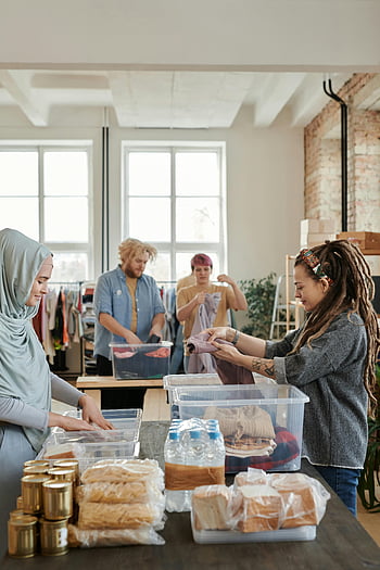 Volontari che ordinano donazioni, Gruppo eterogeneo, Centro di donazione indoor, Smorting dei vestiti, prodotti alimentari, contenitori di plastica, servizio alla comunità, attività di beneficenza, volontariato, Centro di donazione, donazioni di cibo e abbigliamento