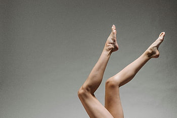 vrouwelijke benen, grijze achtergrond, studio opname, elegante vorm, beweging, verhoogde benen, neutraal grijs, menselijke voeten, Lichtfotografie, artistieke pose, minimalistische fotografie