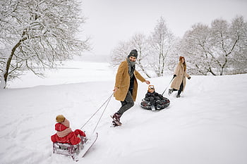 family sledding, snowy forest, winter fun, man pulling sled, woman pulling sled, children sledding, snowy landscape, winter activities, family winter fun, outdoor winter fun, snowy day
