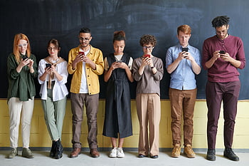 diverse group, adults, standing in a row, engaged with smartphones, blackboard, casual clothing, indoor setting, technology use, social media, group interaction, modern lifestyle