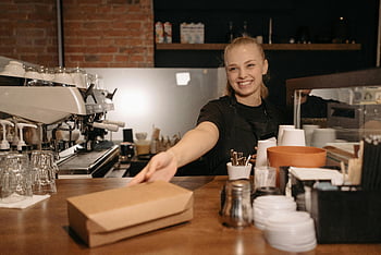 smilende kvinne, Black Crew Neck T-skjorte, utdelingsboks, moderne kaffebar, bartender, Takeout Box, Kaffebardisk, Smilende barista, kaffebar interiør, barista uniform