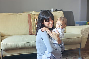 Gri kazakta kadın, yürümeye başlayan çocuk, Beyaz Düğme Gömlek, Anne Bebeği kucaklayan, iç mekan konforu, kanepe, sıcaklık, beraberlik, Aile Anı, ev ortamı, Aşk