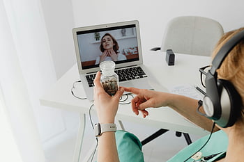 medical professional, video call, remote healthcare, online consultation, clear glass bottle, patient interaction, laptop, headphones, telemedicine, healthcare services, virtual appointment