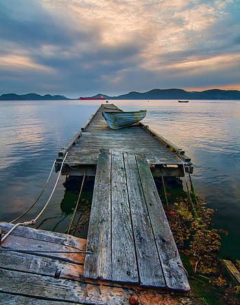 blue boat, gray wooden dock, calm waters, vibrant sunset, peaceful view, wooden jetty, sunset scene, water landscape, serene atmosphere, dockside view, boat on dock