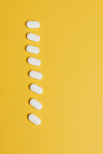 pilules blanches, fond jaune, arrangement vertical, design minimaliste, look moderne, vue de dessus, jaune vibrant, rangée de pilules, capsules blanches, Photographie minimaliste, esthétique moderne