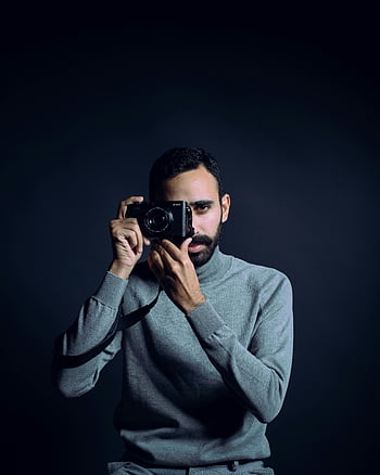 muž v svetr, vousatý fotograf, držení fotoaparátu, Nastavení studia, zachycení okamžiku, portrétní fotografie, tmavé pozadí, profesionální fotograf, ležérní oblečení, fotografování v interiéru, mužského modelu