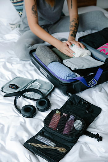 black headphones, toiletries bag, person packing, suitcase, travel preparation, clothes, bed, personal items, preparing for trip, travel essentials, luggage packing
