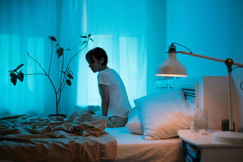 Donna seduta sul letto, camera da letto illuminata di blu, donna contemplativa, solitudine, letto, illuminazione blu, scena notturna, Scena indoor, atmosfera calma, riflessione, cuscino