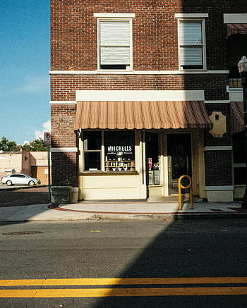 devanture de magasin en briques, Auvent rayé, coin de rue ensoleillé, charme de petite ville, établissement commercial, route en béton, boutique pittoresque, journée ensoleillée, coin de la rue, lignes jaunes, extérieur du bâtiment