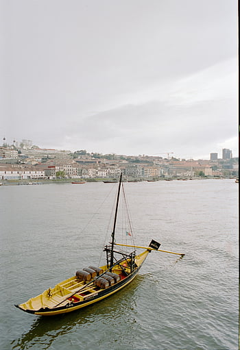 wooden sailboat, Douro River, Porto cityscape, traditional Portuguese boat, city in Portugal, river scene, sailboat on river, port city, urban waterfront, Portuguese culture, maritime tradition