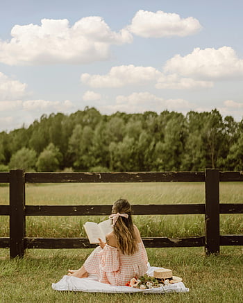 woman reading, picnic blanket, wooden fence, countryside, outdoor reading, nature scene, peaceful setting, rural landscape, summer day, book lover, picnic setup
