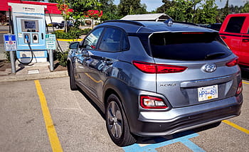 Elektroauto, DC -Ladegerät, Hyundai Kona, Ladestation, Parkplatz, blaues Auto, roter LKW, grüne Bäume, tagsüber, draussen, Fahrzeug