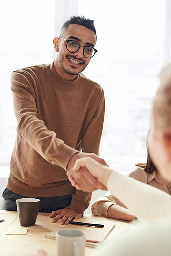 business meeting, handshake, smiling professionals, indoor setting, brown sweater, office environment, professional interaction, business people, friendly gesture, workplace interaction, collaboration