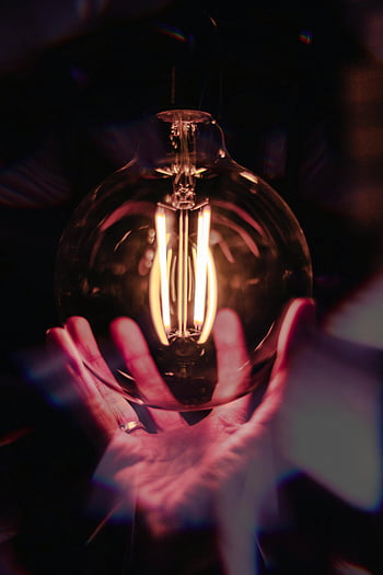close-up photo, person holding bulb, warm glowing filament, light bulb, hands, dramatic effect, artistic effect, filament light bulb, glowing light, artistic photo, dramatic lighting