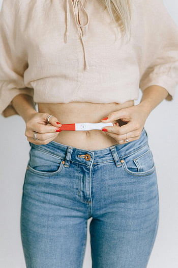 Test di gravidanza positivo, colpo del primo piano, tenuta della donna, momento di felicità, Annuncio di gravidanza, smalto rosso, Abbigliamento casual, Blue jeans, Top beige, parte superiore ritagliata, Risultato del test di gravidanza