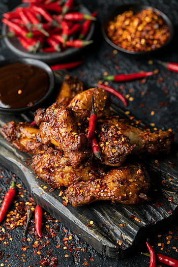 spicy chicken wings, red chilies, wooden surface, flavorful meal, cooked meat, chilies garnish, delicious wings, spicy food, chicken dish, wooden platter, red peppers