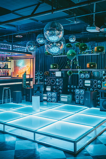 disco koule, noční klub, retro interiér, neonová světla, vinobraní výzdoba, živá atmosféra, taneční parket, reproduktory, televizní přijímače, modré osvětlení, retro výzdoba