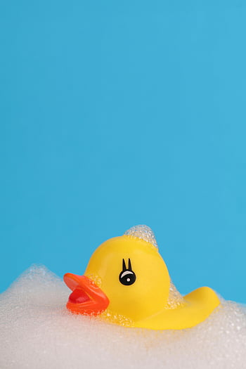 yellow rubber duck, white foam, soap bubbles, bright blue background, cheerful, floating, bath toy, playful, fun, children's toy, bath time