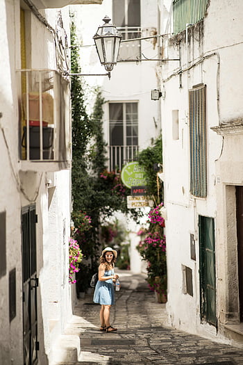 woman standing on pathway, Lecce, Puglia, Italy, historic architecture, vibrant flowers, narrow street, tourist exploring, white houses, street lamp, cobblestone path