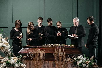 funeral service, family gathering, pastor, solemn setting, indoor funeral, coffin, loss remembrance, adults mourning, floral arrangements, funeral ceremony, memorial service