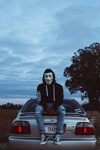 Guy Fawkes mask, silver Honda Civic, hacker mask, Williamsburg VA, person sitting on car, outdoor photo, Virginia license plate, dusk scene, casual outfit, ripped jeans, black hoodie