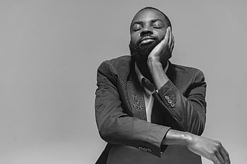 thoughtful man, black and white portrait, studio photography, man with beard, man with eyes closed, hand resting on face, formal attire, grayscale image, introspective expression.