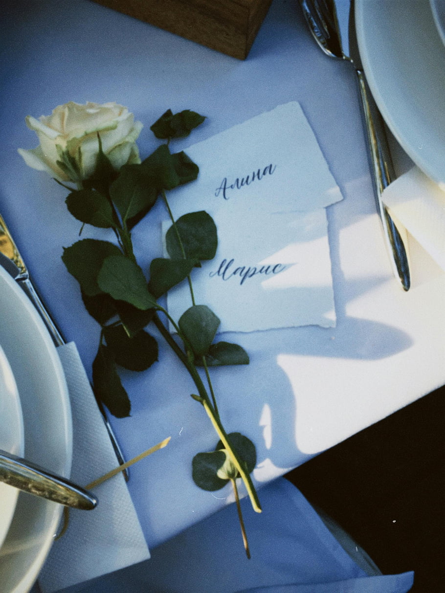 white rose, green leaves, personalized name cards, dining table, elegant table setup, table decoration, event decor, floral arrangement, name tags, table setting, wedding table