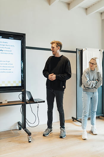 man and woman, standing next, whiteboard, presentation, informal workshop, digital screen, engaged people, workshop setting, presentation setting, whiteboard presentation, digital presentation
