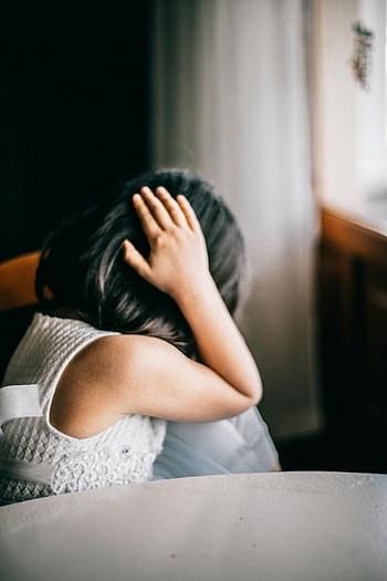 young girl, emotional distress, indoor setting, hand on head, seated position, white dress, indoor environment, emotional state, childhood emotions, distress signal, indoor scene