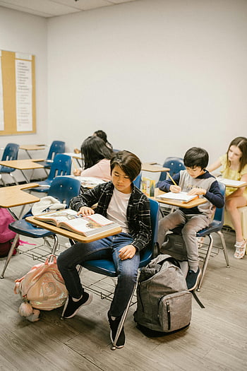 gutt sitter på skrivebordet, lese bok, klasserommet, studenter studerer, innendørs læring, gruppe studenter, Fokusert lesing, skolemiljø, pedagogiske omgivelser, ryggsekker, skrivebord og stoler