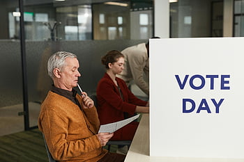 valgdagen, mann som leser stemmeseddelen, innendørs avstemning, valgdag, valglokalet, folk som stemmer, beslutningstaking, stemmeprosess, valgarrangement, velgerdeltakelse, stemmeseddelgjennomgang